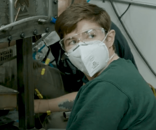 Kate works on the ground surrounded by machinery and wires