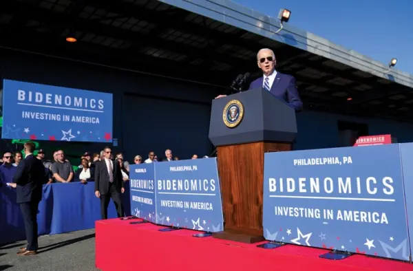 biden makes annoucement at a podium in front of Biden Investment signs